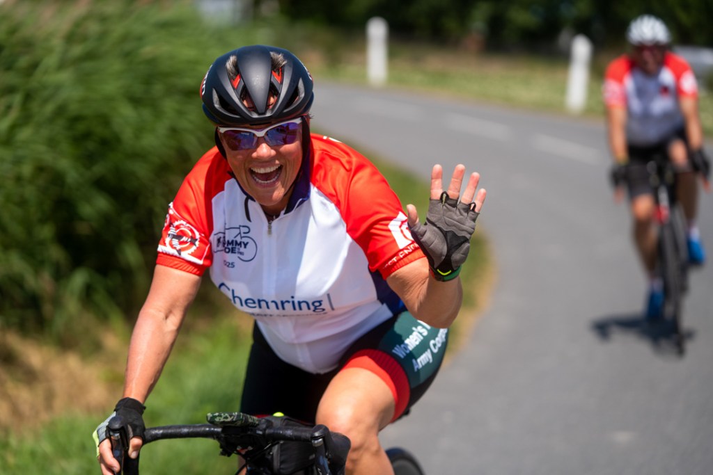 A woman participates in the Tommy Ride - she's waving to the camera while riding her bike