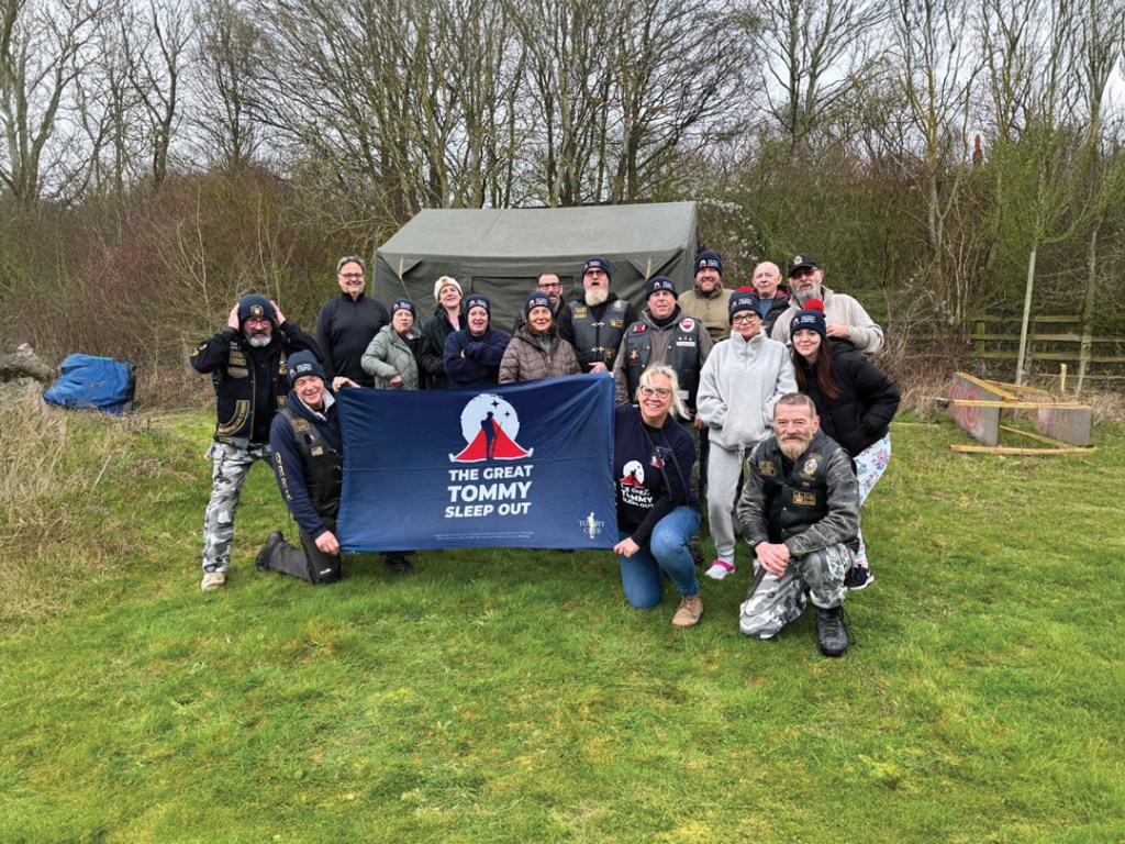 Group of sleep outers holding banner in a field with trees in the background