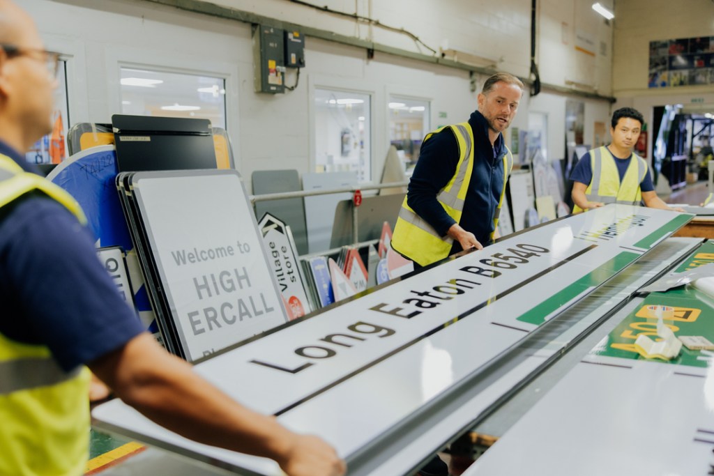 Three veterans lifting Long Eaton traffic sign onto work bench