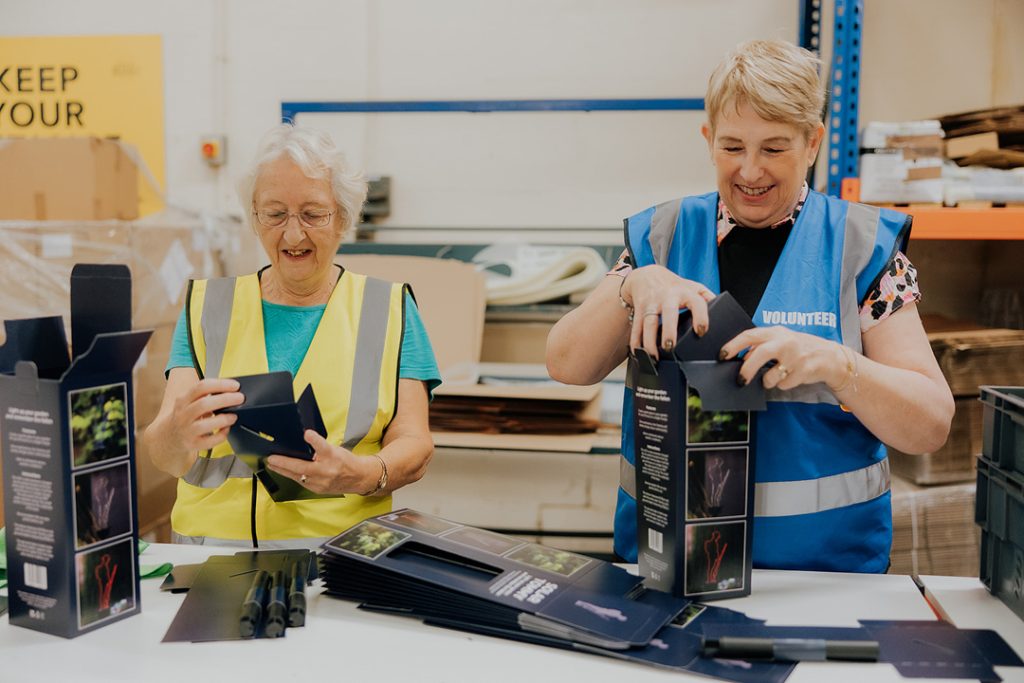 Two women packing Tommy Garden lights as in blue and yellow high visibility jacket